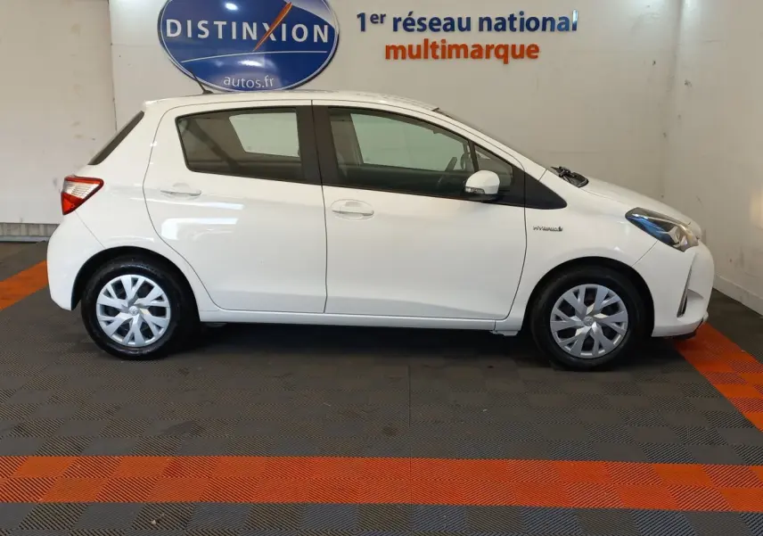 Profil côté gauche d'une Toyota Yaris blanche 2019 hybride, avec jantes standard et logo Hybrid visible sur l'aile avant.