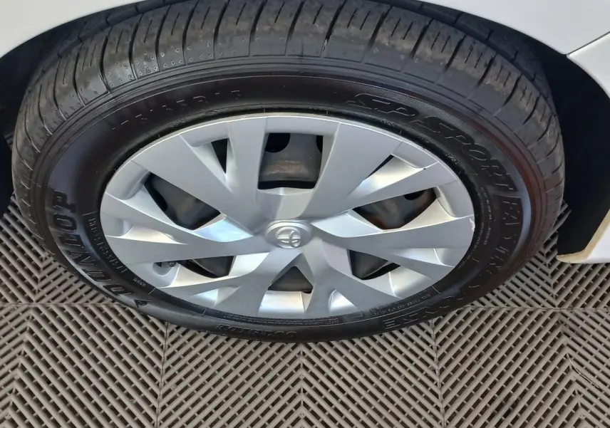 Gros plan sur la roue avant droite d'une Toyota Yaris blanche, avec jante argentée et pneu Dunlop visible.
