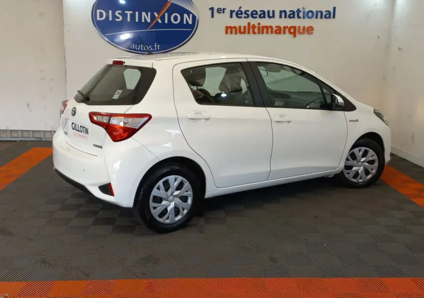 Profil droit d'une Toyota Yaris blanche 2019 hybride, avec jantes standard et logo Distinxion en arrière-plan.