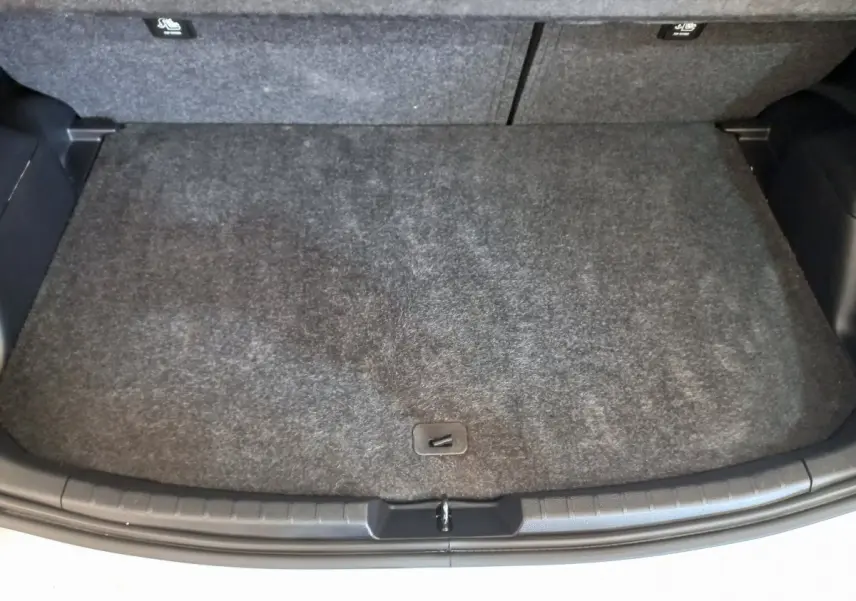 Coffre ouvert d'une Toyota Yaris blanche, vue de dessus montrant la surface de chargement avec tapis gris.