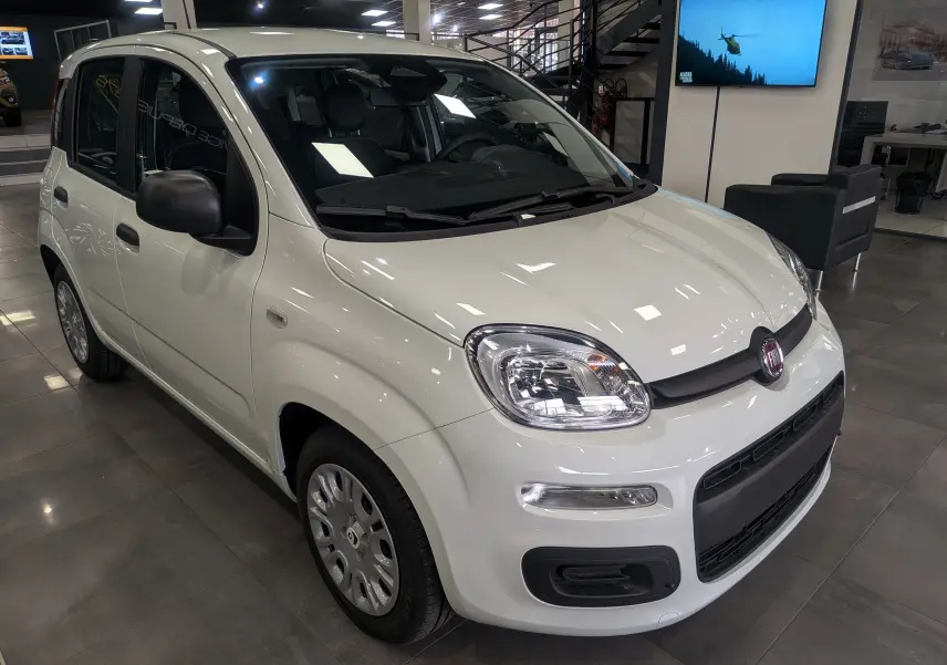 Vue 3/4 avant droite d'une FIAT Panda 1.0 70 CH Hybrid City blanche Gelato en showroom lumineux.