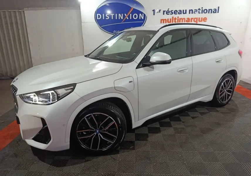 BMW X1 xDrive25e blanc en 3/4 avant droit, avec jantes noires et éclairage LED allumé.