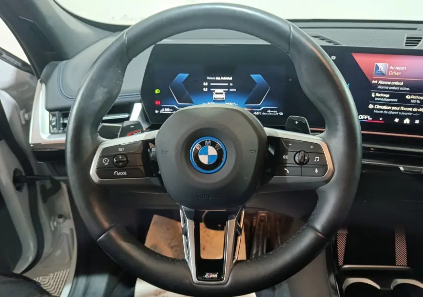 Vue centrée sur le volant cuir noir BMW X1 xDrive25e 2024 avec tableau de bord digital et écran tactile.