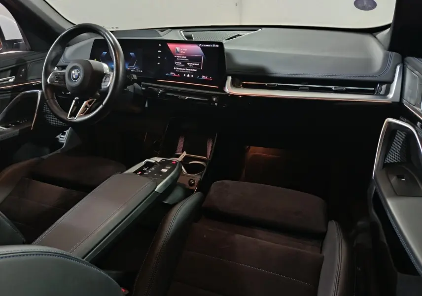 Intérieur BMW X1 xDrive25e 2024 vu de l'avant, tableau de bord noir avec écran tactile large et volant cuir multifonctions.