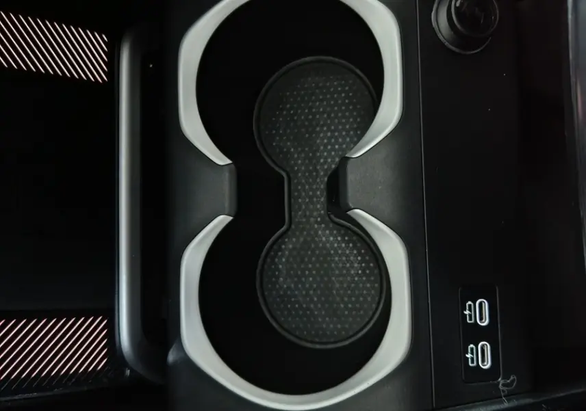 Gros plan sur les porte-gobelets noirs et gris du BMW X1 xDrive25e M Sport 2024, avec commandes éclairées à côté.