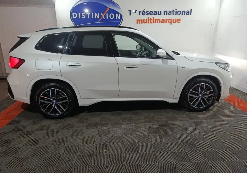 Vue de profil côté gauche d'un BMW X1 blanc xDrive25e M Sport 2024 avec jantes noires et logo M Sport visible.