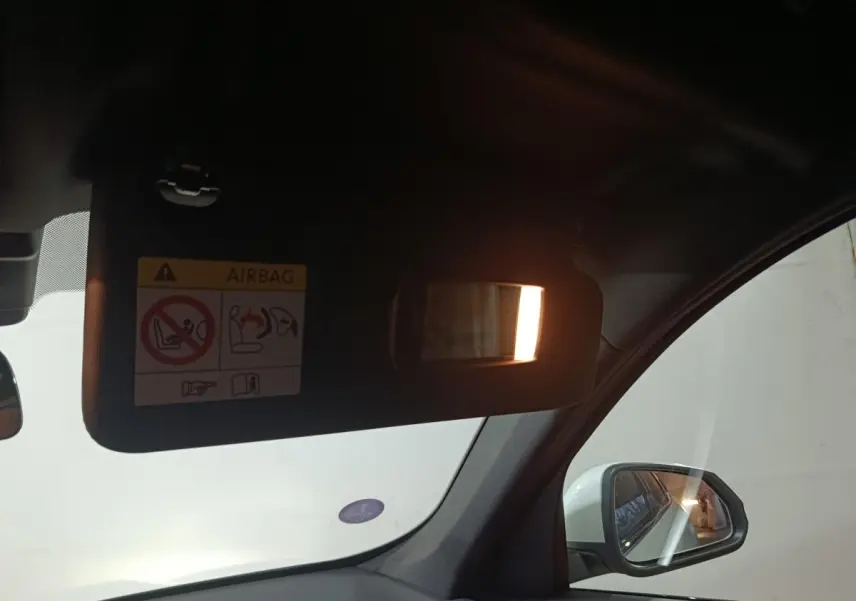 Vue intérieure côté conducteur du BMW X1 blanc 2024, avec pare-soleil baissé et miroir éclairé, rétroviseur extérieur visible.