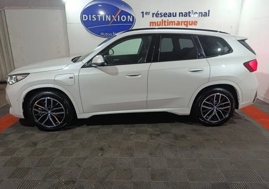 Vue de profil côté gauche d’un BMW X1 blanc xDrive25e M Sport avec jantes noires et logo M sur aile avant.
