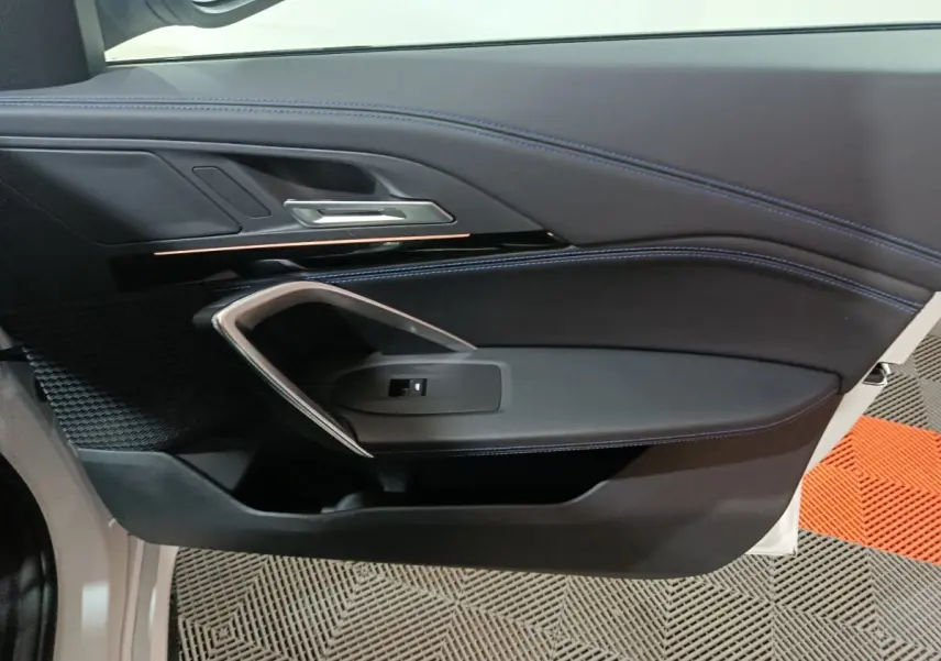 Vue intérieure côté gauche de la porte avant d'une BMW X1 blanche, avec surpiqûres bleues et poignée argentée.