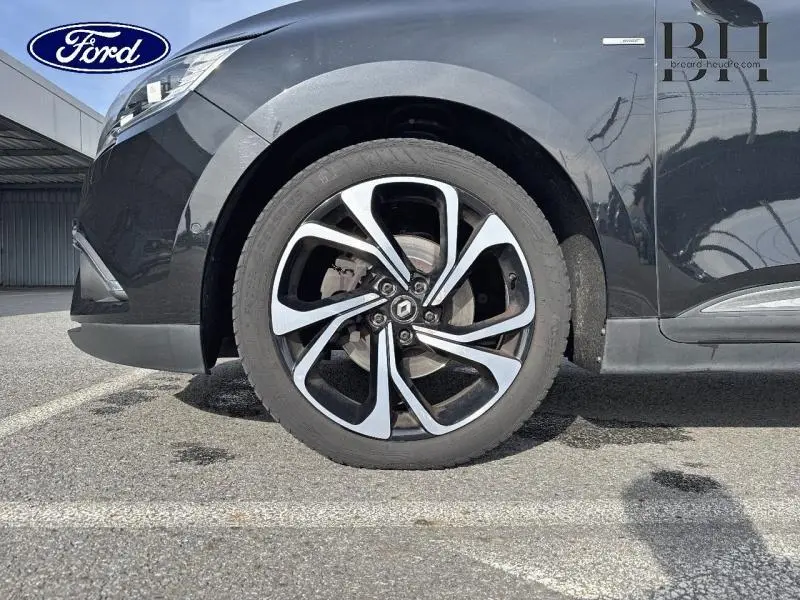 Gros plan sur la roue avant gauche noire étoilée d’un Renault Grand Scenic 2017 avec jante en alliage au design moderne.