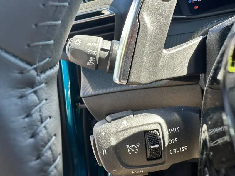 Gros plan sur les commandes au volant du Peugeot 2008 bleu Obsession, montrant les réglages du régulateur de vitesse et des phares.