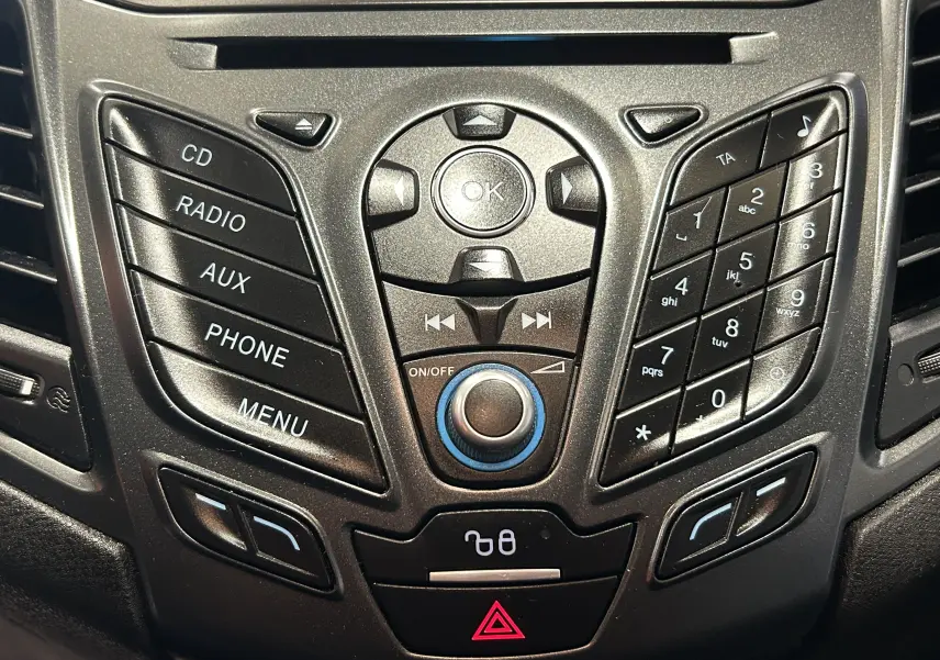 Vue rapprochée du panneau central de commande audio et téléphone de la Ford Fiesta blanche, avec boutons noirs et marquages blancs.