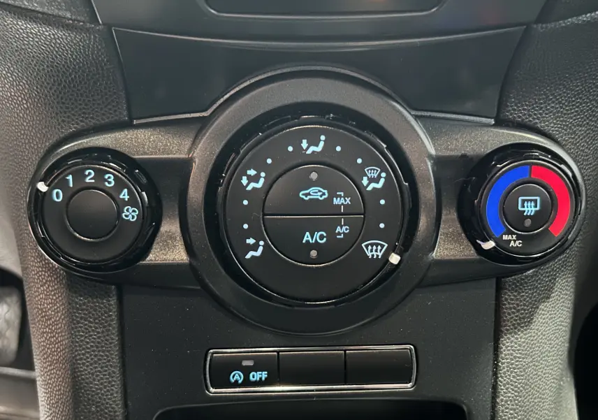 Gros plan sur les commandes de climatisation noires avec réglages bleu et rouge dans une Ford Fiesta blanche de 2015.