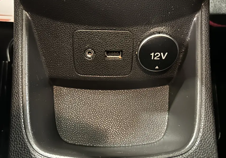 Gros plan sur la prise 12V, port USB et entrée auxiliaire dans l’habitacle noir de la Ford Fiesta blanche EcoBoost 2015.