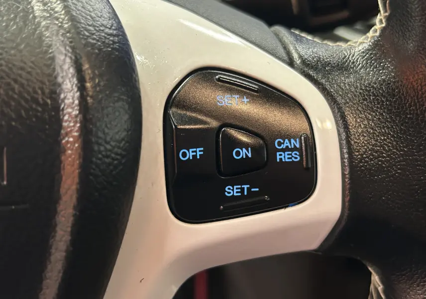Gros plan sur les commandes de régulateur de vitesse à droite du volant noir avec insert blanc d'une Ford Fiesta blanche de 2015.