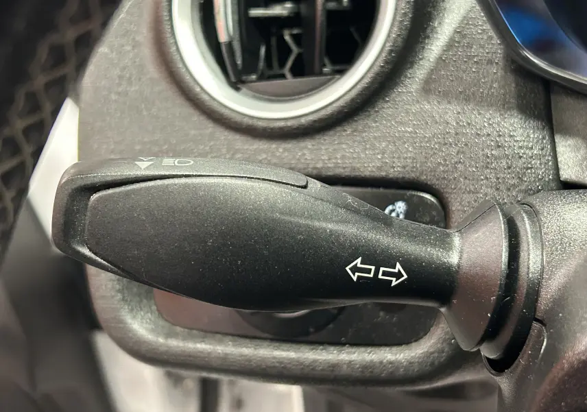 Gros plan sur la commande de clignotant noire à gauche du volant dans l’habitacle d’une Ford Fiesta blanche.