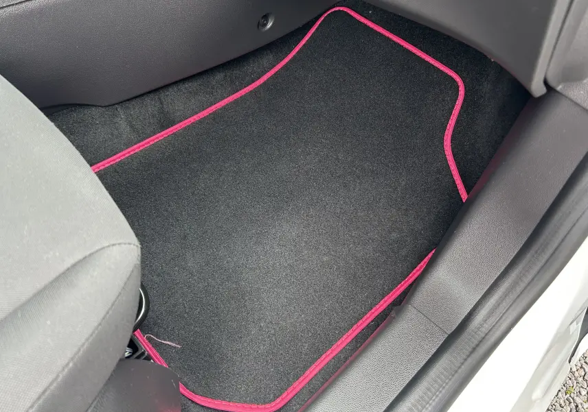 Vue intérieure côté passager avant d'une Ford Fiesta blanche de 2015, avec tapis de sol noir bordé de rose.