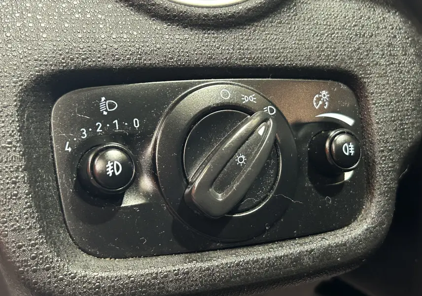 Gros plan sur le bouton de commande des phares et feux antibrouillard du tableau de bord d'une Ford Fiesta blanche.