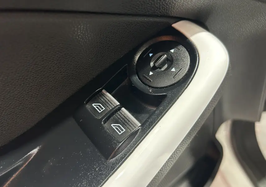 Gros plan sur les commandes de réglage des rétroviseurs et des vitres électriques côté conducteur d’une Ford Fiesta blanche de 2015.