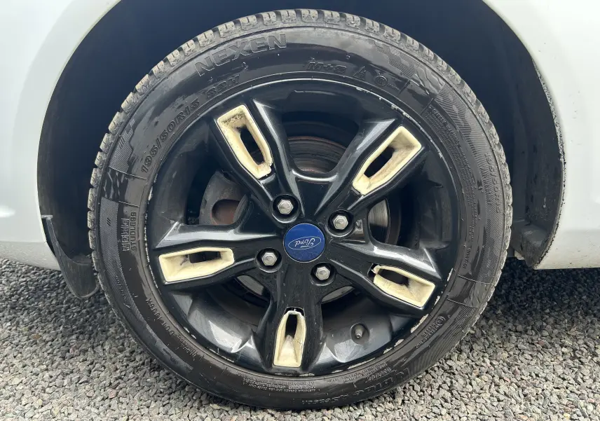 Gros plan sur la jante noire à inserts beige d’une Ford Fiesta blanche, mettant en valeur le logo Ford central.
