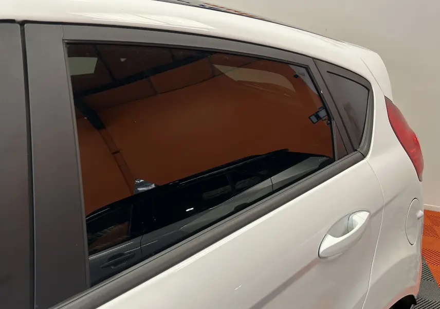 Vue rapprochée du côté arrière droit d'une Ford Fiesta blanche, mettant en valeur la poignée de porte et la vitre teintée.