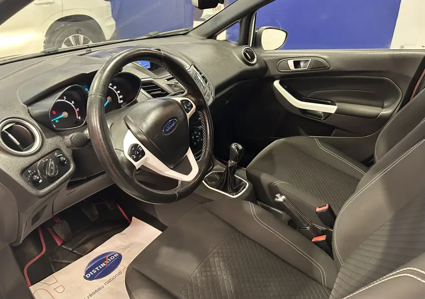 Vue intérieure côté conducteur de la Ford Fiesta 2015 avec volant multifonction et sellerie tissu noire.