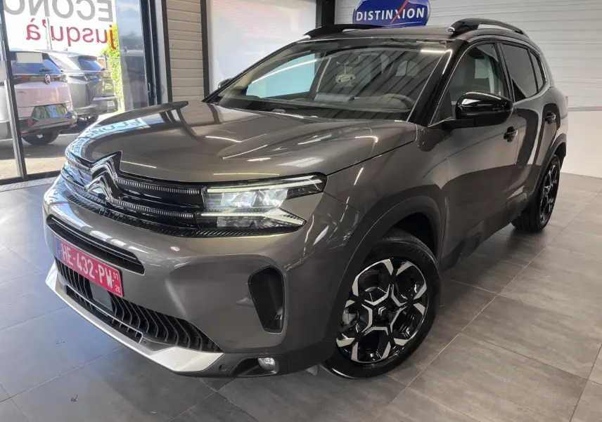 Vue 3/4 avant droite du Citroën C5 Aircross gris platinium avec jantes alliage bi-ton et barres de toit noires.