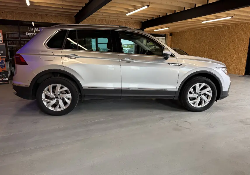 Vue de profil côté gauche d’un Volkswagen Tiguan gris clair hybride rechargeable, dans un garage avec murs en bois.