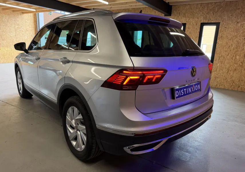 Vue 3/4 arrière droite d’un Volkswagen Tiguan gris clair 2022 avec feux arrière allumés dans un garage.