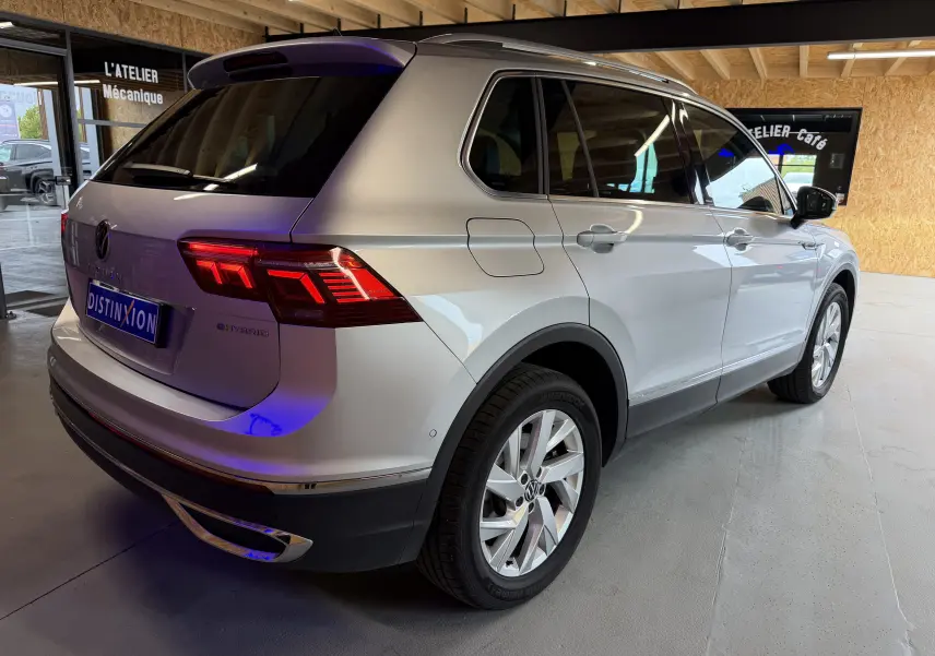 Vue 3/4 arrière droite d'un Volkswagen Tiguan gris clair hybride rechargeable avec feux arrière LED allumés en intérieur d'atelier.