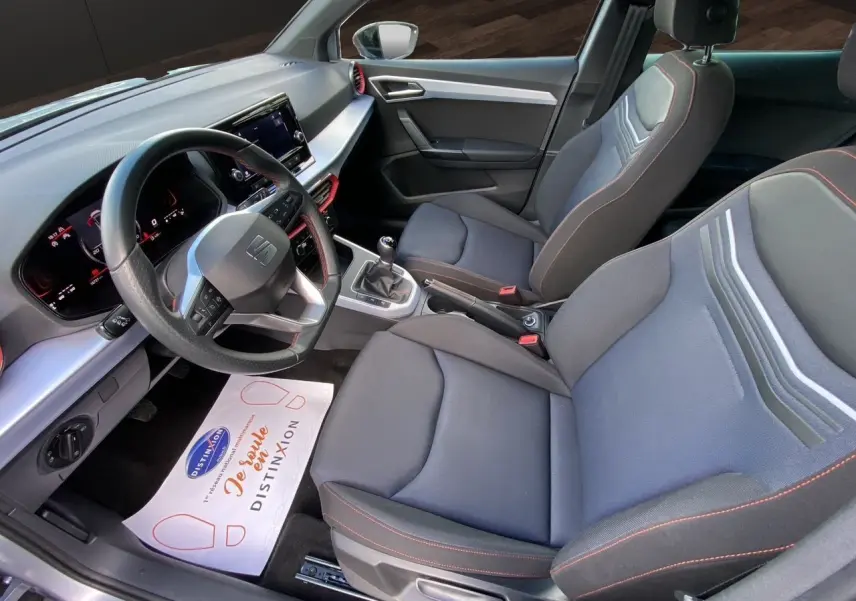 Intérieur avant droit du SEAT Arona 2024 avec sièges tissu noirs à surpiqûres rouges et tableau de bord digital.