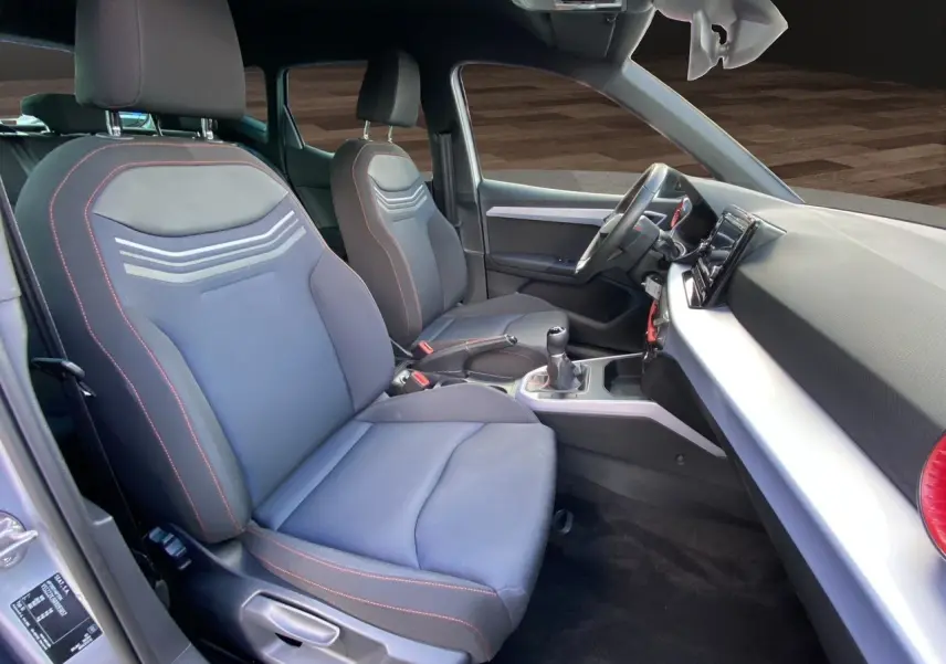 Intérieur avant du SEAT Arona 2024, vue côté gauche, sièges tissu noir avec surpiqûres rouges et tableau de bord moderne.