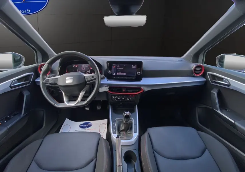 Intérieur avant du SEAT Arona 2024 avec volant multifonction, écran tactile central et sellerie noire en tissu.