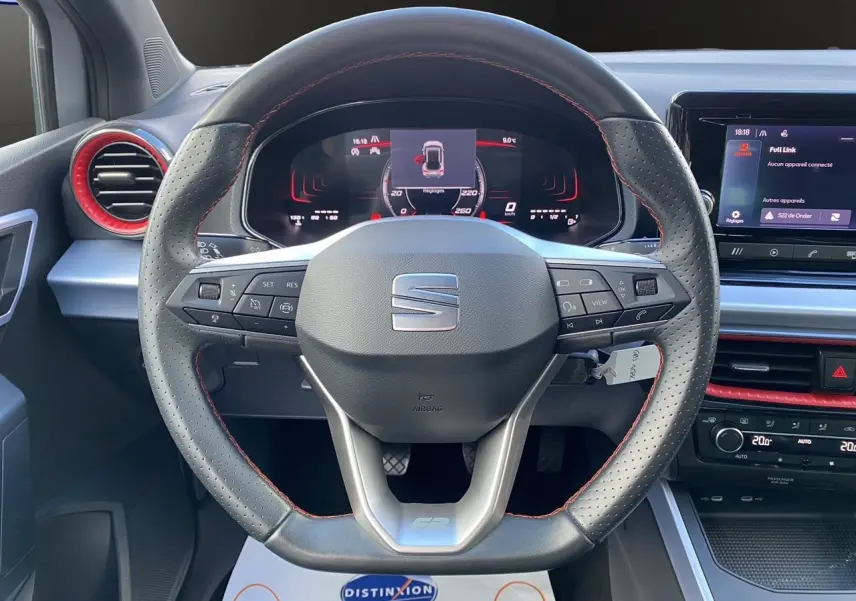 Volant perforé avec surpiqûres rouges et tableau de bord digital d'une SEAT Arona gris silver intérieur noir, vue de face.