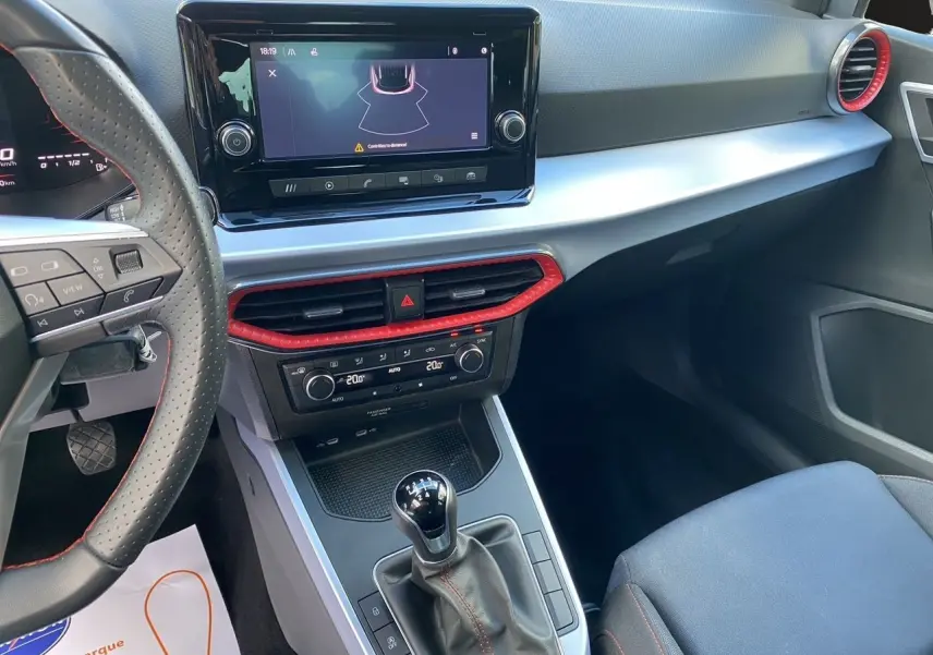Vue intérieure du tableau de bord et console centrale d'une SEAT Arona 2024 avec boîte manuelle, garnitures noires et touches rouges.