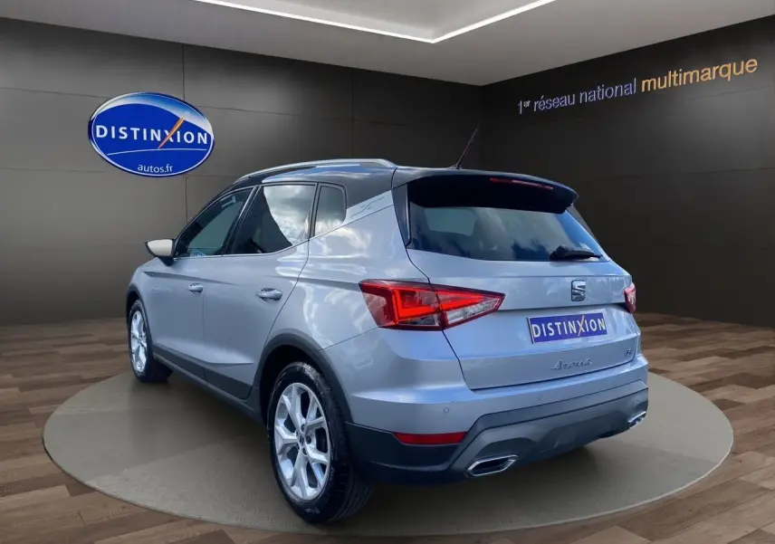 Vue 3/4 arrière droite d'un SEAT Arona gris silver avec toit noir et jantes alu 17 pouces dans un showroom.