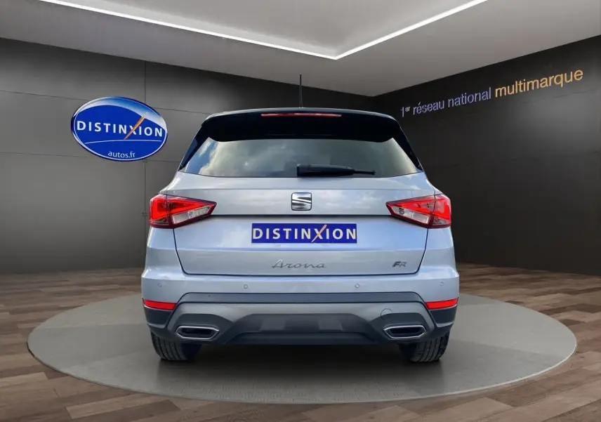 Vue arrière d'une SEAT Arona gris silver avec toit noir et double sortie d'échappement intégrée, en intérieur showroom.