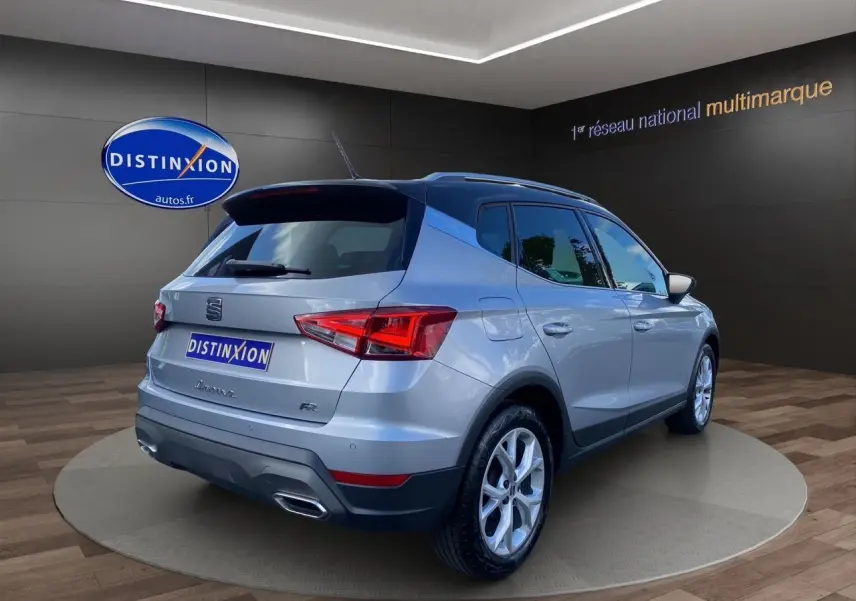 Vue 3/4 arrière droite d'un SEAT Arona gris silver avec toit noir et jantes alu 17 pouces dans un showroom.