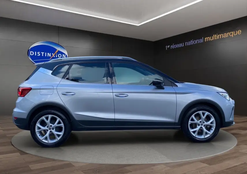 Vue de profil côté gauche du SEAT Arona gris silver avec toit noir et jantes alu 17 pouces en intérieur showroom.