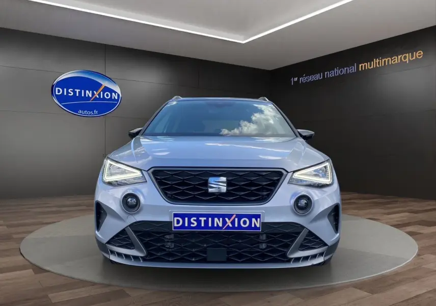 Vue frontale d'un SEAT Arona gris silver avec toit noir, feux LED allumés et calandre noire en showroom.