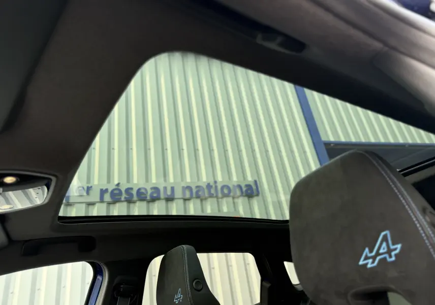 Vue intérieure du toit panoramique et appui-tête avant avec logo Alpine bleu du Renault Austral 2025 bleu Iron toit noir.