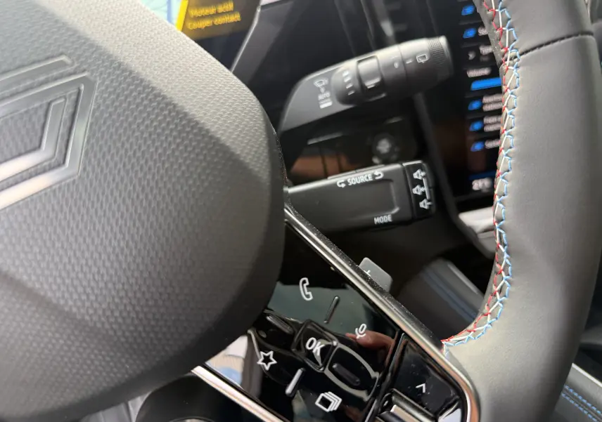 Gros plan sur le volant cuir noir à surpiqûres tricolores du Renault Austral 2025 hybride, avec commandes intégrées.