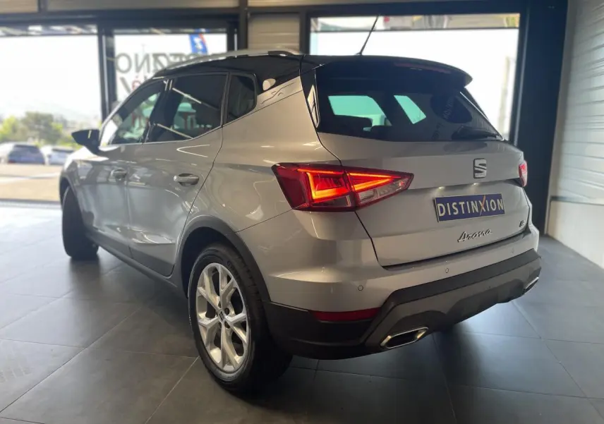 Vue 3/4 arrière droite d'un SEAT Arona 2024 rouge passion avec feux arrière allumés en showroom.