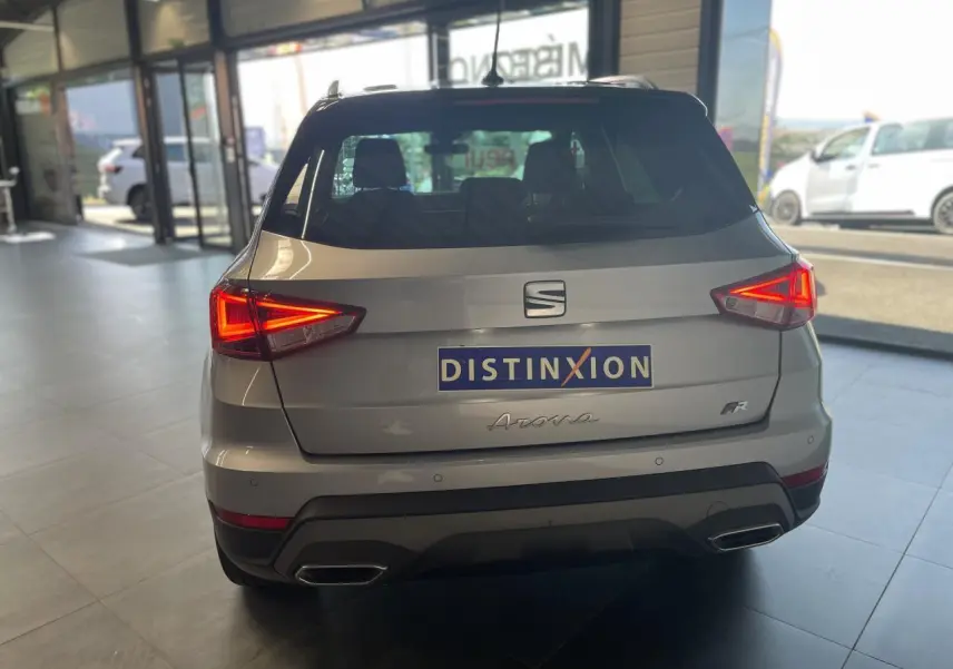 Vue arrière d'un SEAT Arona gris GRS 2024 avec feux allumés et logo FR dans un showroom lumineux.