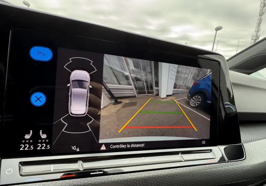 Écran multimédia montrant la caméra de recul d'une Volkswagen Golf blanche 3/4 arrière droite en stationnement.