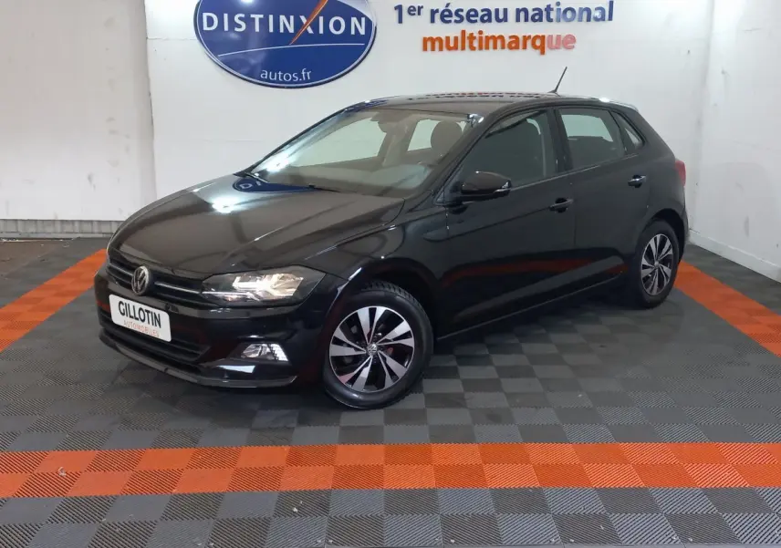 Volkswagen Polo noire vue en 3/4 avant droit dans un showroom avec sol gris et bandes orange.