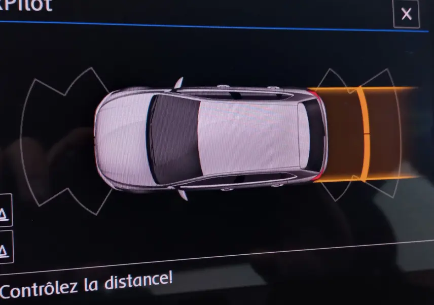 Vue de dessus d'une Volkswagen Polo blanche sur l'écran de stationnement avec alertes de proximité arrière en orange.