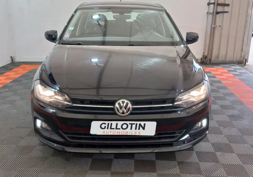 Vue frontale d'une Volkswagen Polo noire 2020 avec phares et feux diurnes allumés en intérieur showroom.