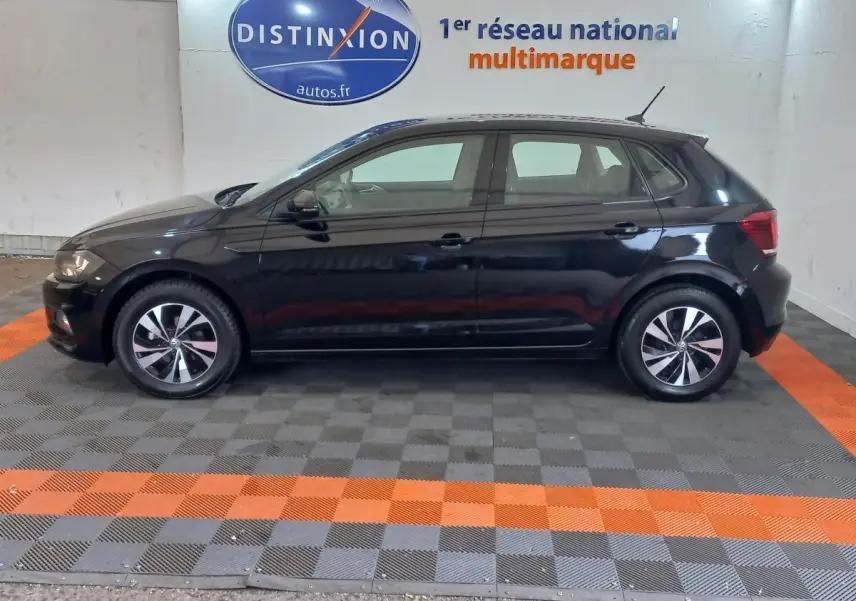 Profil côté gauche d'une Volkswagen Polo noire 2020 stationnée en intérieur sur un sol à damiers gris et orange.