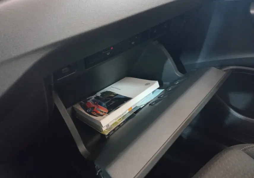 Vue intérieure du coffre à gants ouvert de la Volkswagen Polo noire, avec manuel et documents visibles à l'intérieur.